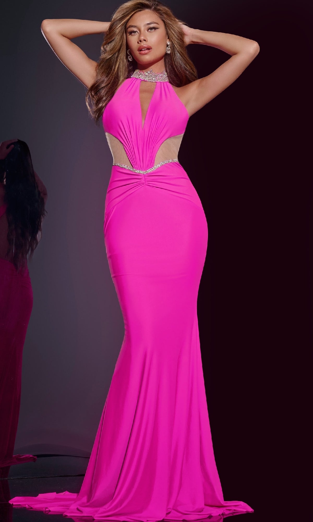 A woman poses in the Jovani D5022, a bright pink long prom dress featuring an embellished halter neckline, cut-out sides, rhinestone details, and an open back, set against a dark background.